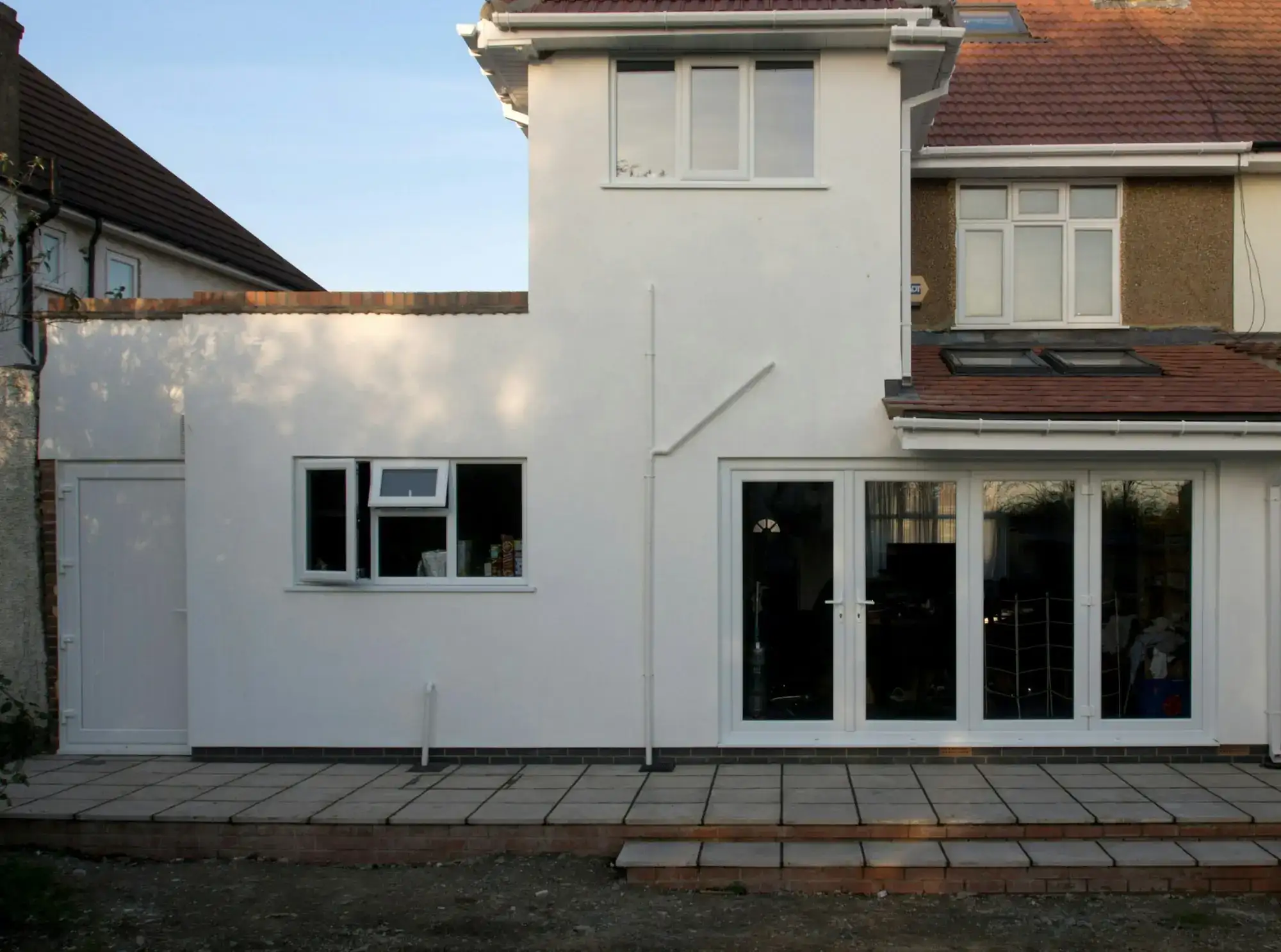 The same back of the house after the work: a new white extension, glass doors and a stone patio (stock photo)