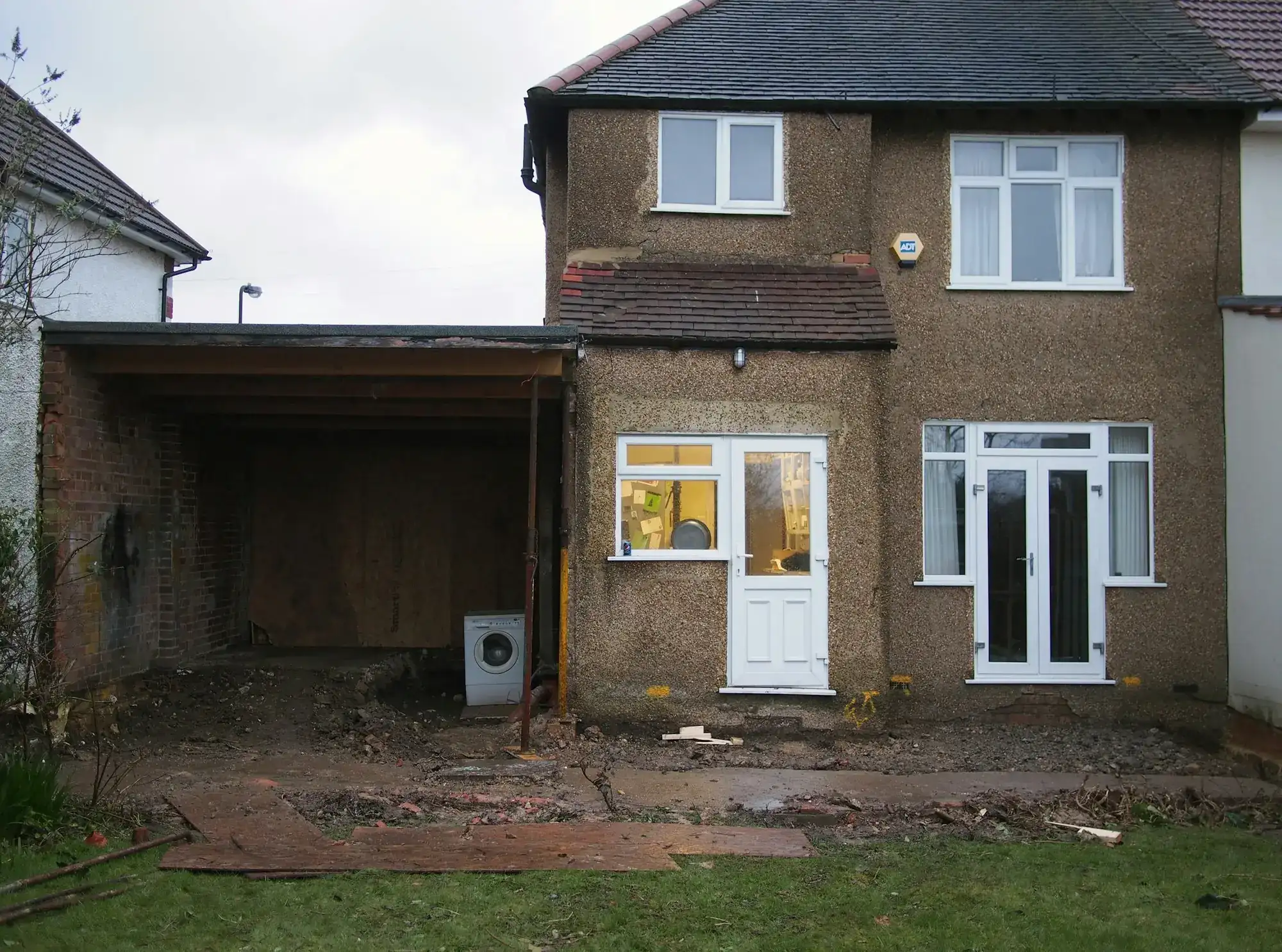 The back of a house before the work: a bare carport, a dirt yard and old pebble-dash walls (stock photo)