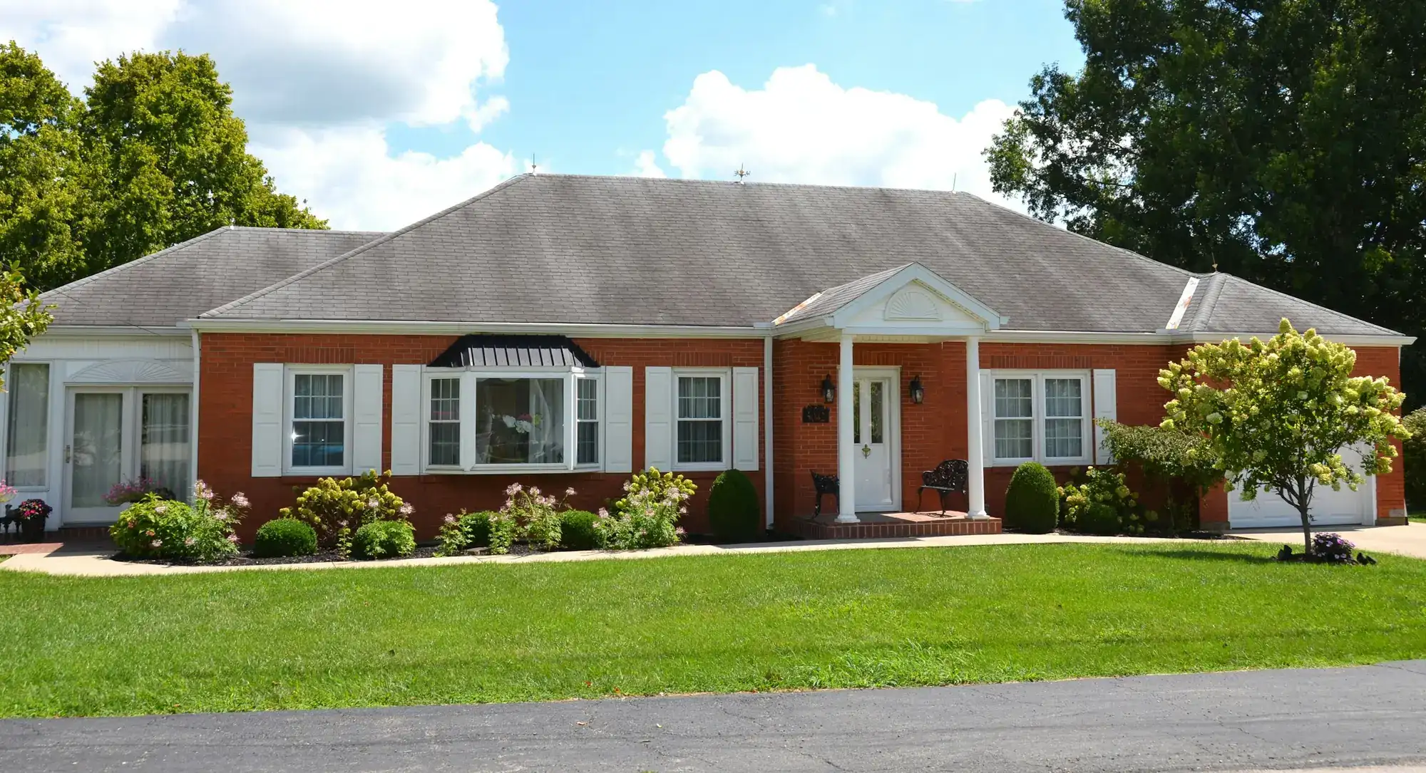 A one-story brick ranch house with white shutters and a green lawn (stock photo)