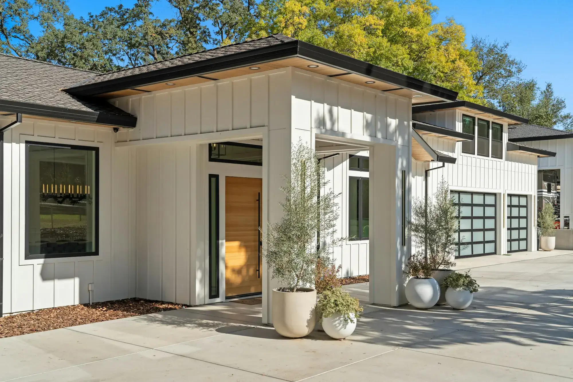 A modern white farmhouse with a wood front door and potted olive trees (stock photo)